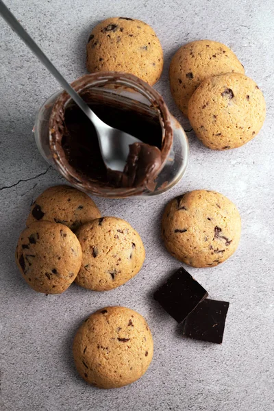 Blurred image of cookies and a jar of chocolate paste and a spoon on a gray table. Snack concept.