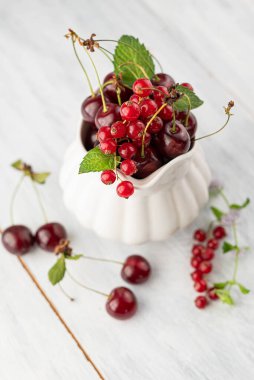 Kırmızı üzümlerin ve kirazların bulanık görüntüsü beyaz bir sürahi içinde ışıklı bir masada..