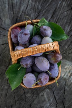 Tahta bir arka planda hasır sepette olgun erikler. Yukarıdan görüntüle.