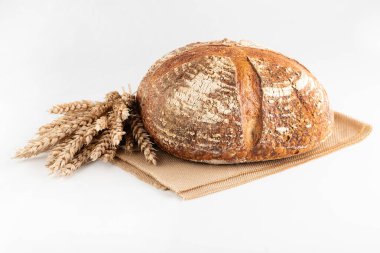 Beyaz arka planda yuvarlak ekmek ve bir demet buğday kulağı var..
