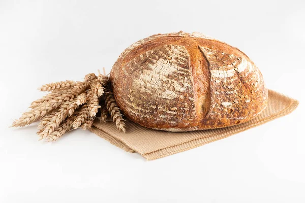 Beyaz arka planda yuvarlak ekmek ve bir demet buğday kulağı var..