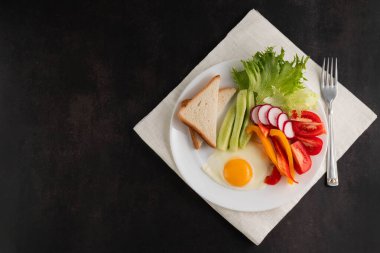 Koyu bir masada, beyaz bir tabakta çırpılmış yumurta, taze sebze ve tost var. Düzgün beslenme kavramı.