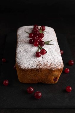 Koyu bir arka planda, kek pudra şekerle serpilmiş ve yaban mersini ve biberiye ile süslenmişti..