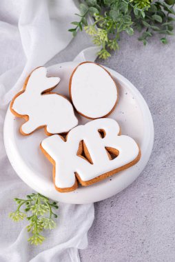 Gri bir masada bir tabak zencefilli paskalya kurabiyesi var. Tavşan, yumurta ve harf şeklinde..