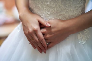 Gelinin elleri, gelinliğin üzerinde, önünde katlanmış.