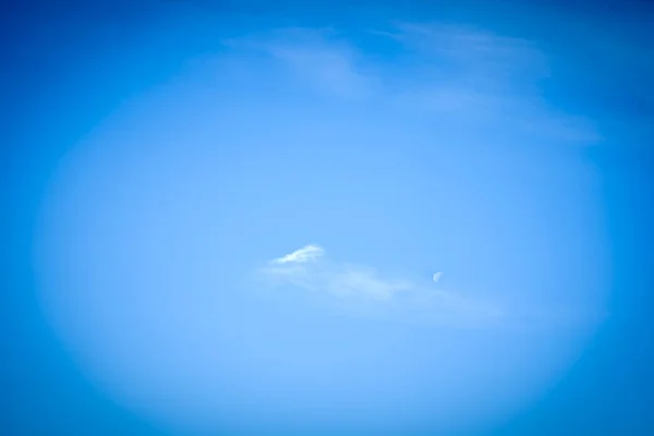 A photo of a small moon and clouds against a deep blue sky