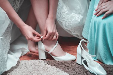Gelinin, gelinlik içinde düğün ayakkabısı giyerken yakın çekimi.