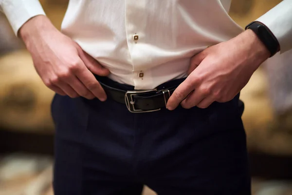 stock image A young man adjusts the belt on his trousers close-up