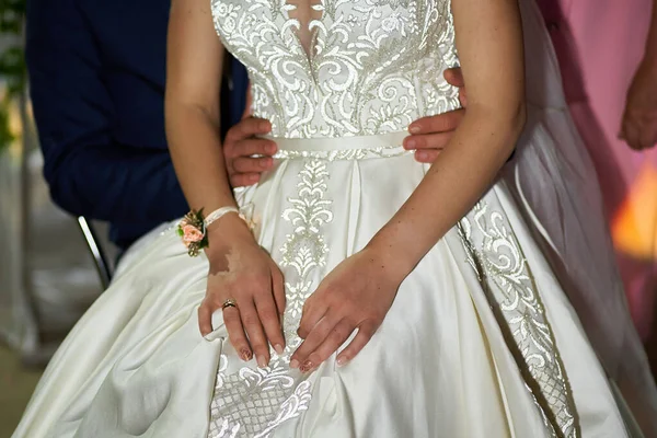 Gelinin, damadın kollarında güzel bir gelinlik içinde otururken yakın çekimi.