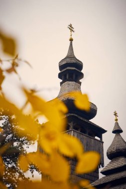 Bir Hıristiyan kilisesinin dikey yakın plan fotoğrafı mavi gökyüzü arkaplanı ve ön plandaki sarı yaprakların çözünmüş hali.