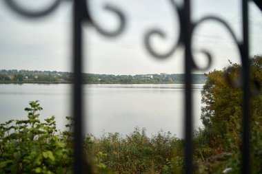 Bulutlu havada göl manzarası. Ön planda tırabzan var.