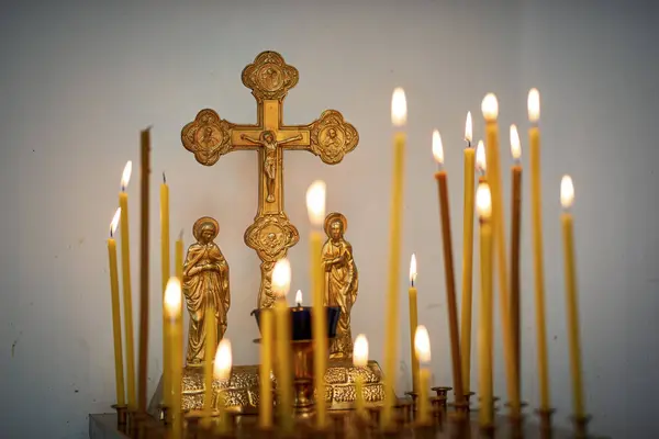 Kilisenin haçı ve yanan mumları kilisedeki beyaz bir duvarın arkasında.