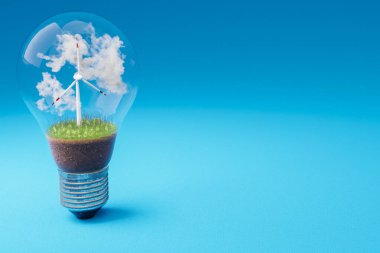 içinde minyatür rüzgar türbini olan tek bir ampul; yeşil toprak ve bulutlar; yenilenebilir enerji konsepti; 3 boyutlu illüstrasyon