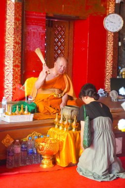 Woman kneeling in fron tof a monk at the gold Temple in Wat Prathat Doi Suthep, Thailand clipart