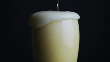 Bardağa bira dolduruyorum. Bira köpüğü dolup taşar ve siyah arkaplanda biter. 