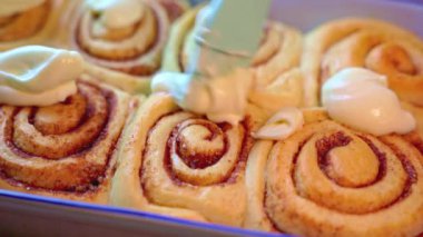 Tarçınlı ruloları tatlı bir peynirle kaplamak için fırça kullanın..