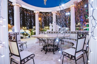 Aydınlatılmış çardak kış gecesi karını aydınlatıyor. Tatil çardağı. Noel Işıkları bir evin dışında