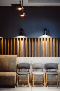 Sakin pastel renkler ve basit çizgilerle modern iç mekan. Duvarın karşısında duran üç gri sandalye retro lambalarla aydınlatılıyor. Oturma odası iç dizayn kompozisyonu. Modern ev dekorasyonu