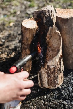 Hand holds manual gas burner near firewood. Man makes a fire on vacation, soft focus