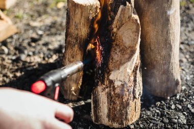 Hand holds manual gas burner near firewood. Man makes a fire on vacation, soft focus