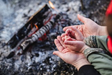 Mom with baby basking by the fire. Close up of baby's hands in mom's hands. Love between child and mother. Mother's day concept. Family. The man warming hands near the bonfire. Film noise