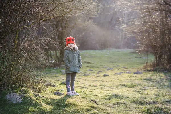 Caucasian little girl in walks in the park in the rays of the setting sun. A child in a red hat walks in a magical fairy-tale spring forest.