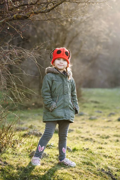 Caucasian little girl in walks in the park in the rays of the setting sun. A child in a red hat walks in a magical fairy-tale spring forest.