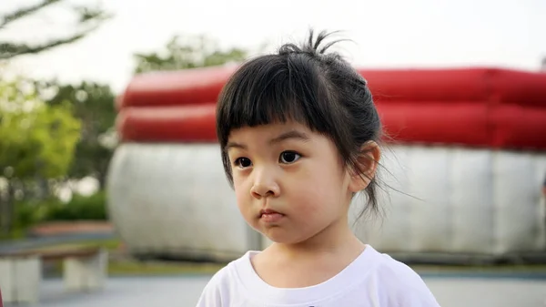 亚洲小女孩心不在焉地站在操场上 特写小孩的特写 亚洲小女孩在户外操场上 田野浅浅的深处 亚洲儿童在室外背景下摆姿势的图像 — 图库照片