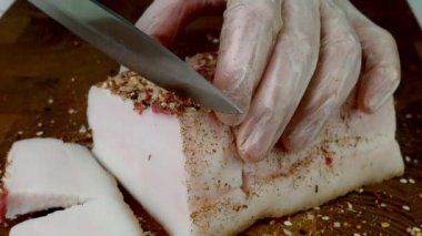 Chef cut raw pork lard on wooden kitchen board with sharp kitchen knife. Salted pork lard traditional Ukrainian cuisine. Close up.