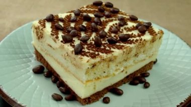 Slice of cream biscuit cake with butter cream decorated with chocolate candies. Rotate on dessert dish on burlap background. Close up.