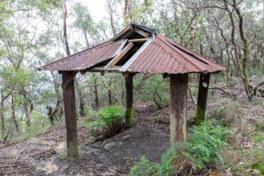 Photograph of an old shelter with wooden support legs and a damaged brown rusty roof in The Blue Mountains in New South Wales in Australia