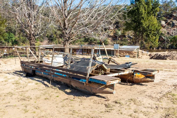 Photograph of a severely flood damaged boat on a white sandy area of land near the Hawkesbury river in New South Wales in Australia