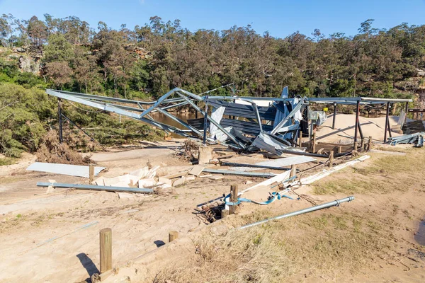 Photograph of a severely flood damaged outdoor building on a white sandy area of land near the Hawkesbury river in New South Wales in Australia