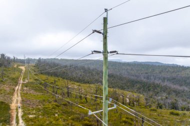 Çevreci ahşap bir elektrik direğinin hava aracı fotoğrafı. Çok sayıda iletim kablosu ve konnektörü var.