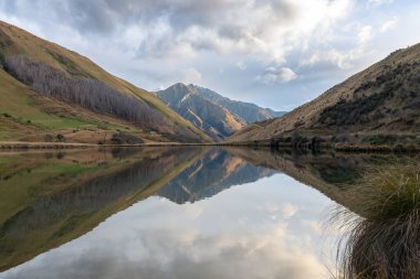 Kirkpatrick Gölü 'nün, Yeni Zelanda' nın Güney Adası 'ndaki Queenstown dışında bulutlu bir günde suya yansıyan dağlarla çekilmiş fotoğrafı.