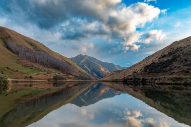 Kirkpatrick Gölü 'nün, Yeni Zelanda' nın Güney Adası 'ndaki Queenstown dışında bulutlu bir günde suya yansıyan dağlarla çekilmiş fotoğrafı.