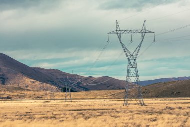 Yeni Zelanda 'nın Güney Adası' ndaki mavi gökyüzüne karşı uzanan büyük aktarım kulelerinin ve hatların fotoğrafı.