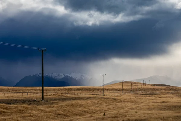 ニュージーランド南島の雪に覆われた山々に対して谷を走る電信柱の写真 — ストック写真