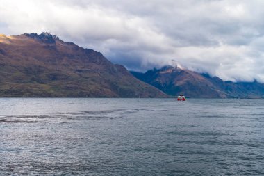 Queenstown 'daki Wakatipu Gölü' ndeki kırmızı ve beyaz bir feribotun fotoğrafı. Yeni Zelanda 'nın Güney Adası' nın arka planında dağlar var.