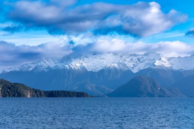 Fiordland 'daki Te Anau' dan Yeni Zelanda 'nın güney adasındaki Manapouri' ye giderken büyük mavi bir göl ve karla kaplı bir dağ sırasının fotoğrafı.