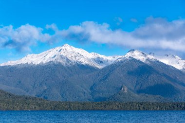 Fiordland 'daki Te Anau' dan Yeni Zelanda 'nın güney adasındaki Manapouri' ye giderken büyük mavi bir göl ve karla kaplı bir dağ sırasının fotoğrafı.