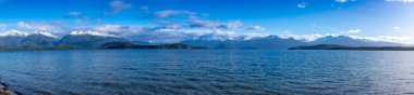 Fiordland 'daki Te Anau' dan Yeni Zelanda 'nın güney adasındaki Manapouri' ye giderken büyük mavi bir göl ve karla kaplı bir dağ sırasının fotoğrafı.