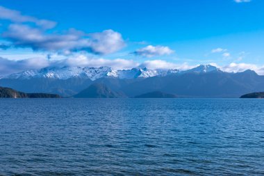 Fiordland 'daki Te Anau' dan Yeni Zelanda 'nın güney adasındaki Manapouri' ye giderken büyük mavi bir göl ve karla kaplı bir dağ sırasının fotoğrafı.