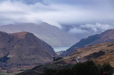 Yeni Zelanda 'nın güney adasındaki Queenstown' da bulutlu bir günde geniş ve dolambaçlı bir vadi boyunca uzanan bir dağ sırası ve gölün Coronet Tepesi 'nden fotoğraf