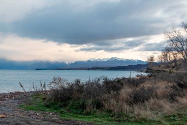 Pukaki Gölü 'nün fotoğrafı, bulutlu bir günde, arka planda kar örtülü dağlarla Yeni Zelanda' nın Güney Adası 'nda.