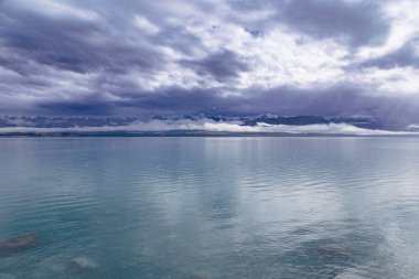 Tekapo Gölü 'nün fotoğrafı. Yeni Zelanda' nın güney adasının arka planında kar örtülü dağlar var.