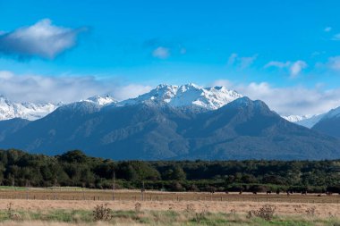 Fiordland 'daki Te Anau' dan Yeni Zelanda 'nın güney adasındaki Manapouri' ye giderken tarımsal otlakların ve dağ manzarasının fotoğrafı.