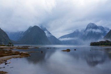 Fotoğraf, Yeni Zelanda 'nın güney adasındaki Fiordland Ulusal Parkı' ndaki tekne limanından bulutlu ve yağmurlu bir günde Milford Sound 'a bakıyor.