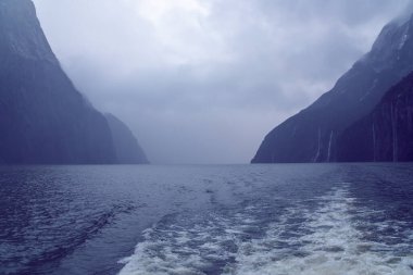 Yeni Zelanda 'nın Güney Adası' ndaki Fiordland Ulusal Parkı 'ndaki Milford Sound' da bulutların ve sisin içindeki dağların fotoğrafı.