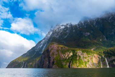 Yeni Zelanda 'nın Güney Adası' ndaki Fiordland Ulusal Parkı 'ndaki Milford Sound' da bulutların ve sisin içindeki dağların fotoğrafı.